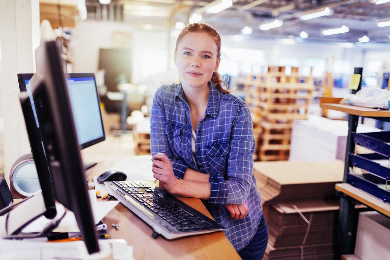 Woman in front of computer monitors with stockroom in background