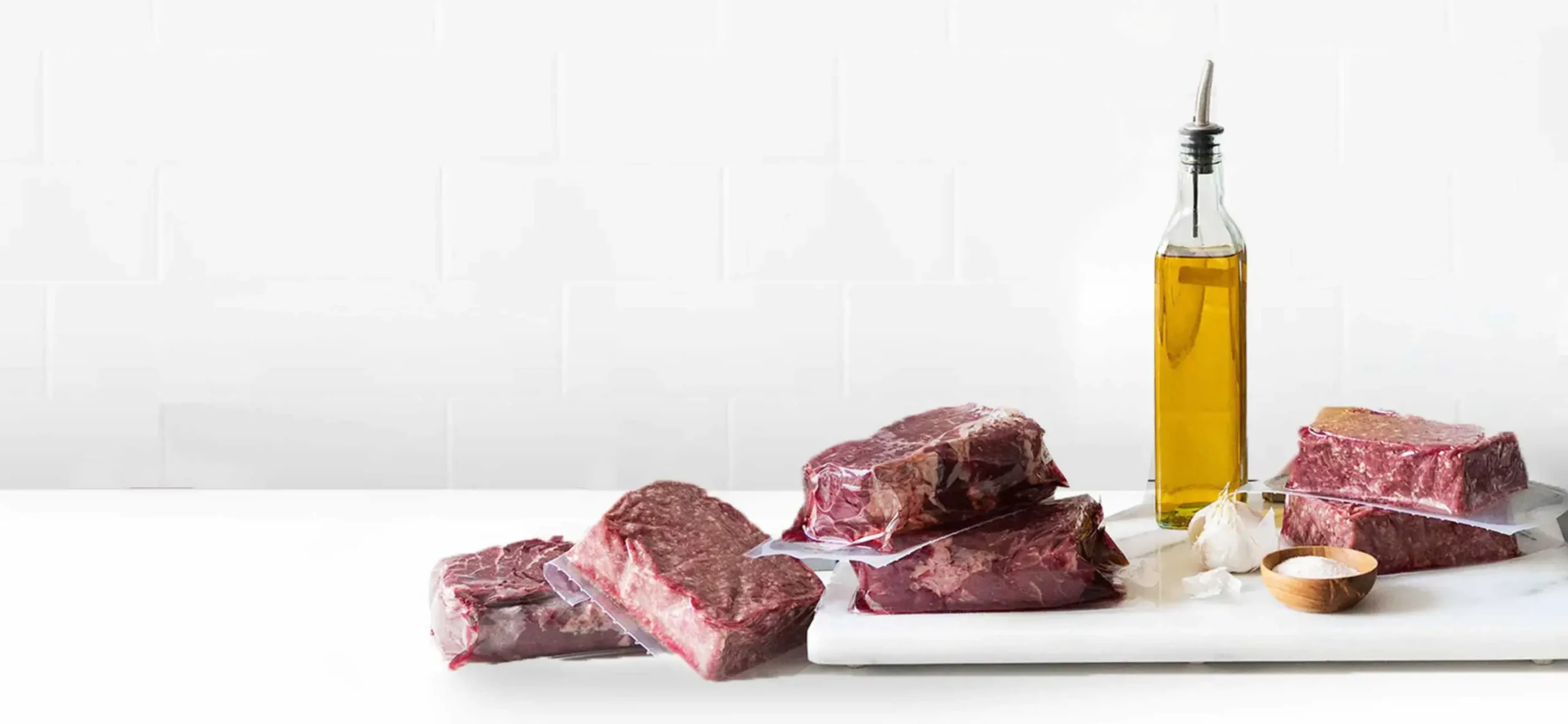 Pre Brands steaks on a white counter with olive oil in the background